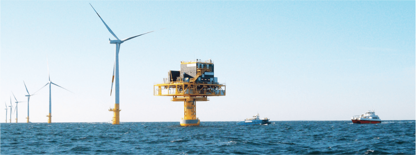oil platform in the middle of the sea with wind energy generators behind on the left.