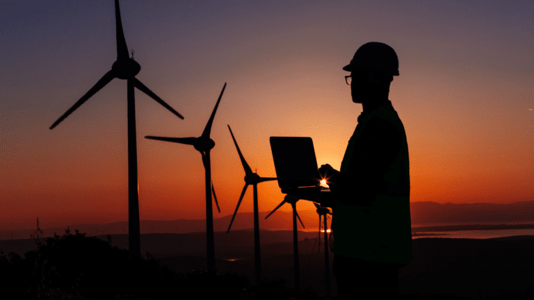Engineer working at a wind farm producing energy. He is doing so during the sunset after working for long hours. His job has the latest technology in use.