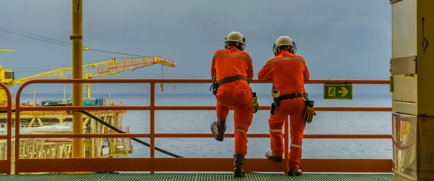 Two men in orange safety gear looking at the ocean from an oil platform