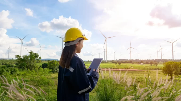 Woman in yellow hard hat looking at a green field with white wind turbines