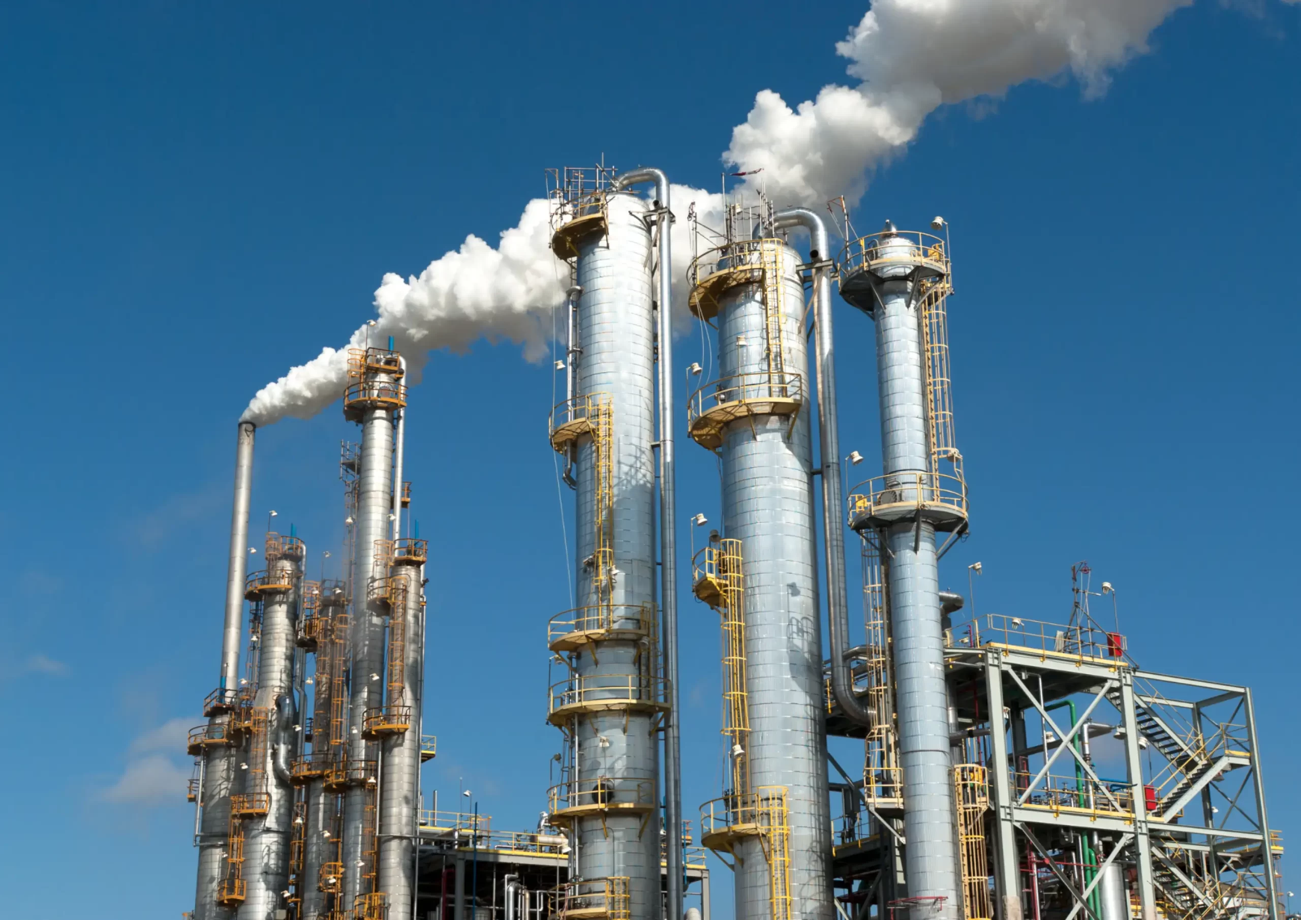 Industrial refinery towers emitting steam under blue sky, showcasing operations and maintenance services in Kenya.