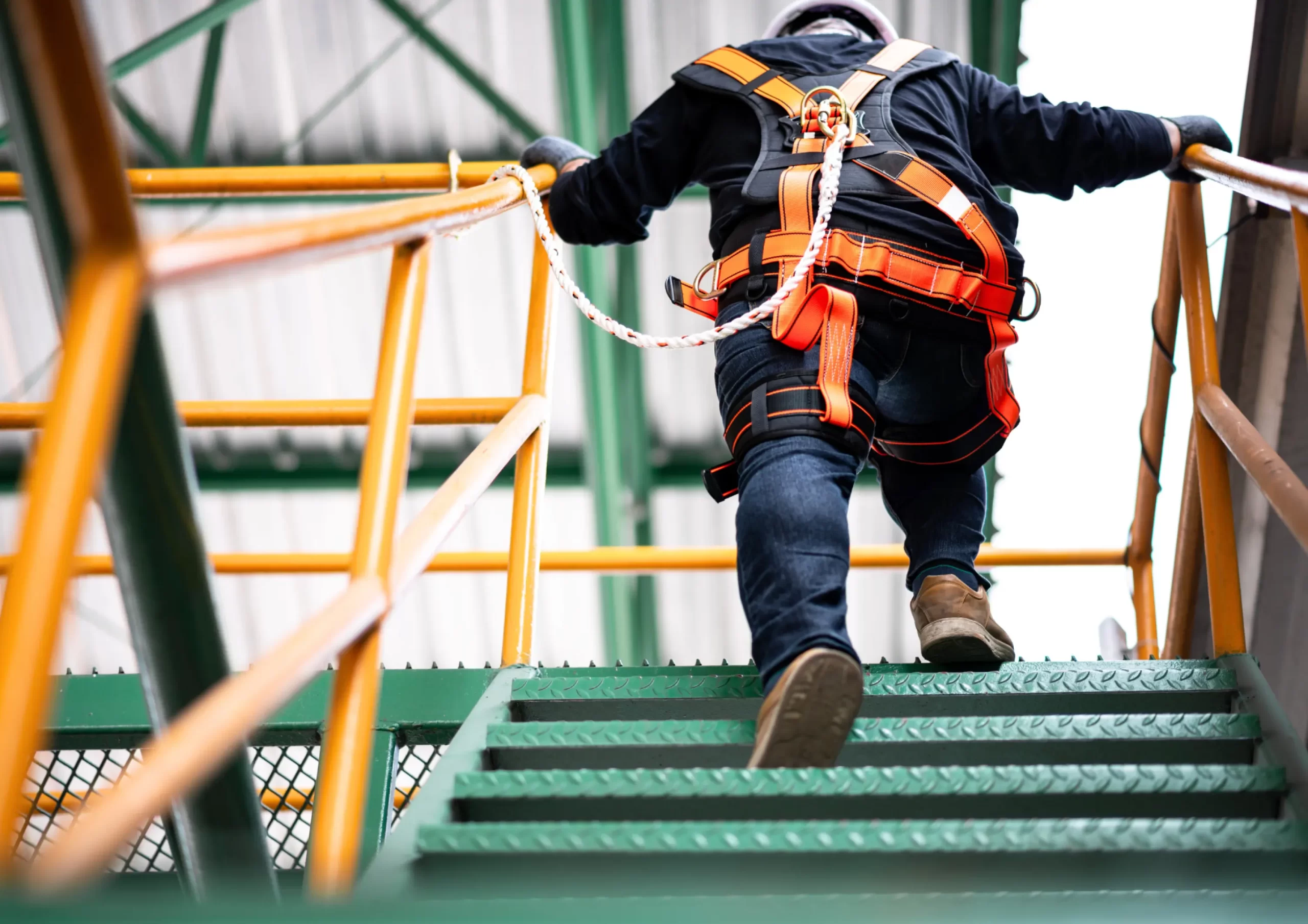 Worker wearing a safety harness climbing stairs at an oil and gas facility during operations and maintenance activities.